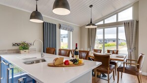Eine moderne Küche mit einer großen Kochinsel, Essbereich mit Holzkästen und großen Fenstern mit Blick ins Freie.