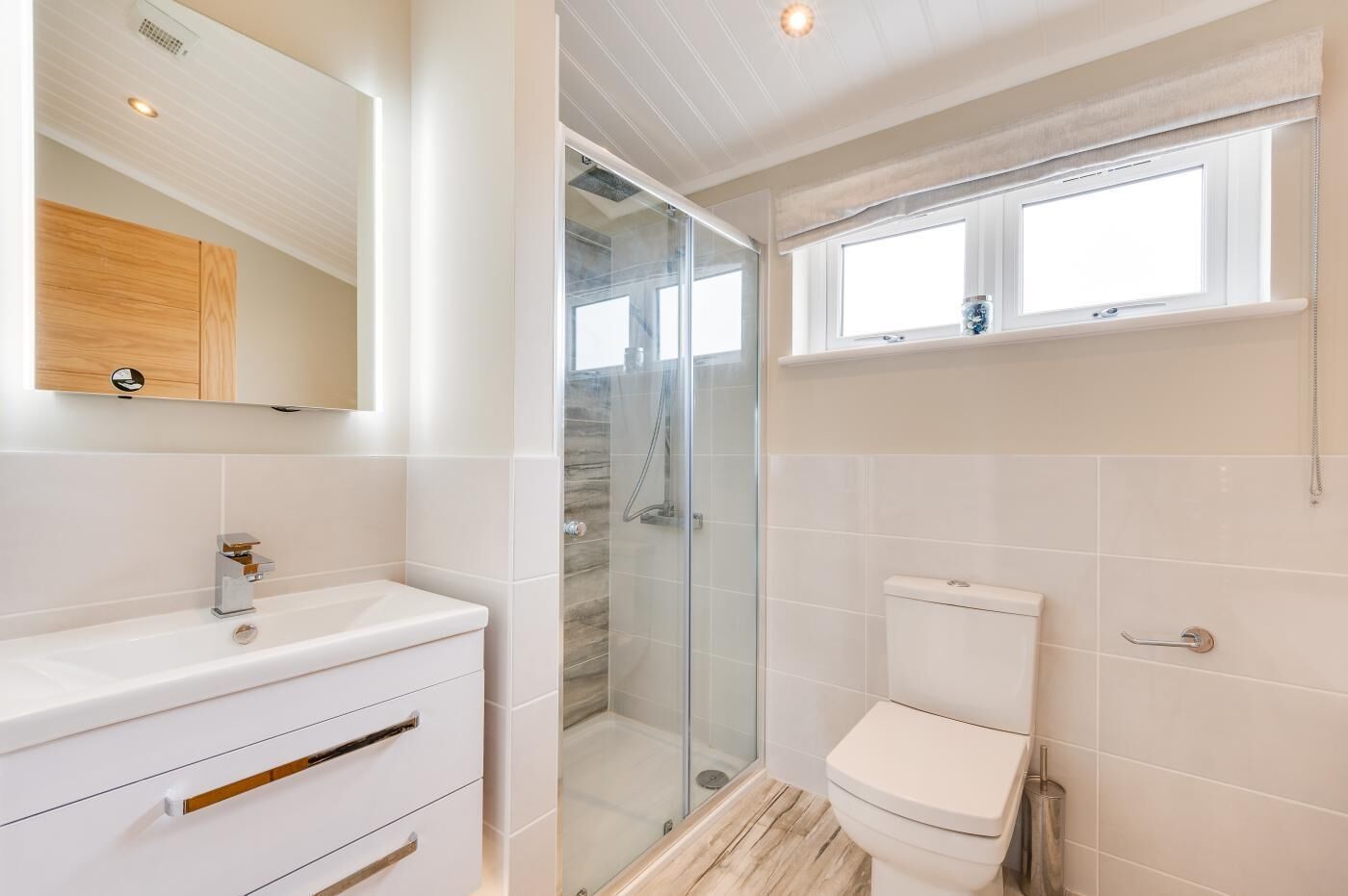 A modern bathroom with a glass shower enclosure, a white toilet, and a vanity with drawers.