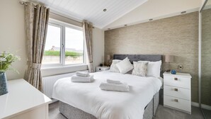 Ein modernes Hotelzimmer mit einem großen Bett, Nachttischen, einem Fenster mit Vorhängen und Blick auf Grünfläche.