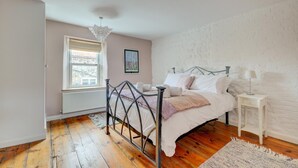 Une chambre à coucher avec un lit en métal, une fenêtre avec des stores, un mur blanc et un radiateur.