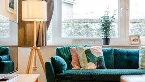 Ein grünes Sofa mit mehreren Kissen, eine Stehlampe und ein Schild mit der Aufschrift 'BEACH' in einem Zimmer mit Fenster.