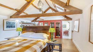 A bedroom with a wooden ceiling, a bed with a checkered blanket, two lamps, and a red door in the background. - 4 Bed in Pateley Bridge (oc-s34135) (Pateley Bridge)
