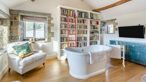 A room with a bathtub, a white sofa, a bookshelf, and a television. - 4 Bed in Pateley Bridge (oc-s34135) (Pateley Bridge)