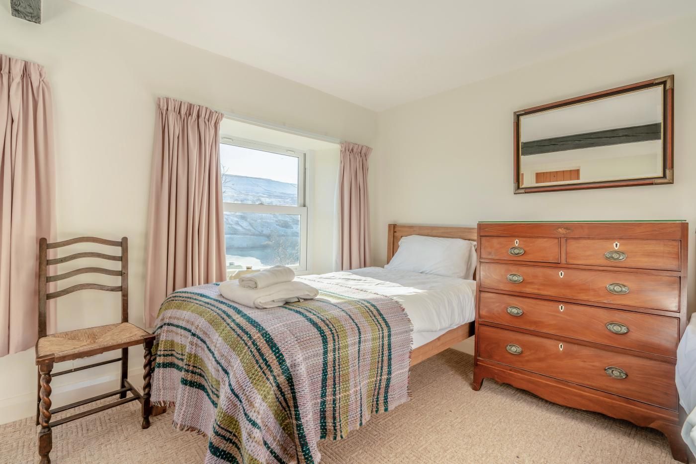A bedroom with a bed, a wooden dresser, a chair, and a window with curtains.