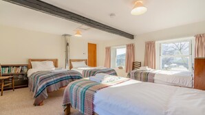 Habitación de hotel con tres camas, una estantería, una ventana con cortinas y una viga de techo de madera.