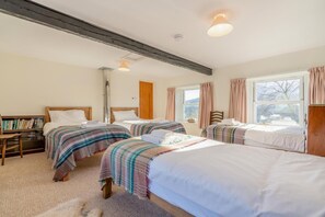 Ein Hotelzimmer mit drei Betten, einem Bücherregal, einem Fenster mit Vorhängen und einem Holzbalken an der Decke.