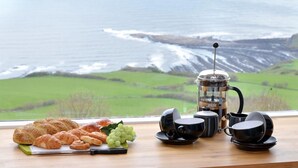 A breakfast setup with croissants, grapes, and a coffee maker on a table with a scenic view of the ocean. - 3 Bed in Scarborough (oc-sa004) (Ravenscar)