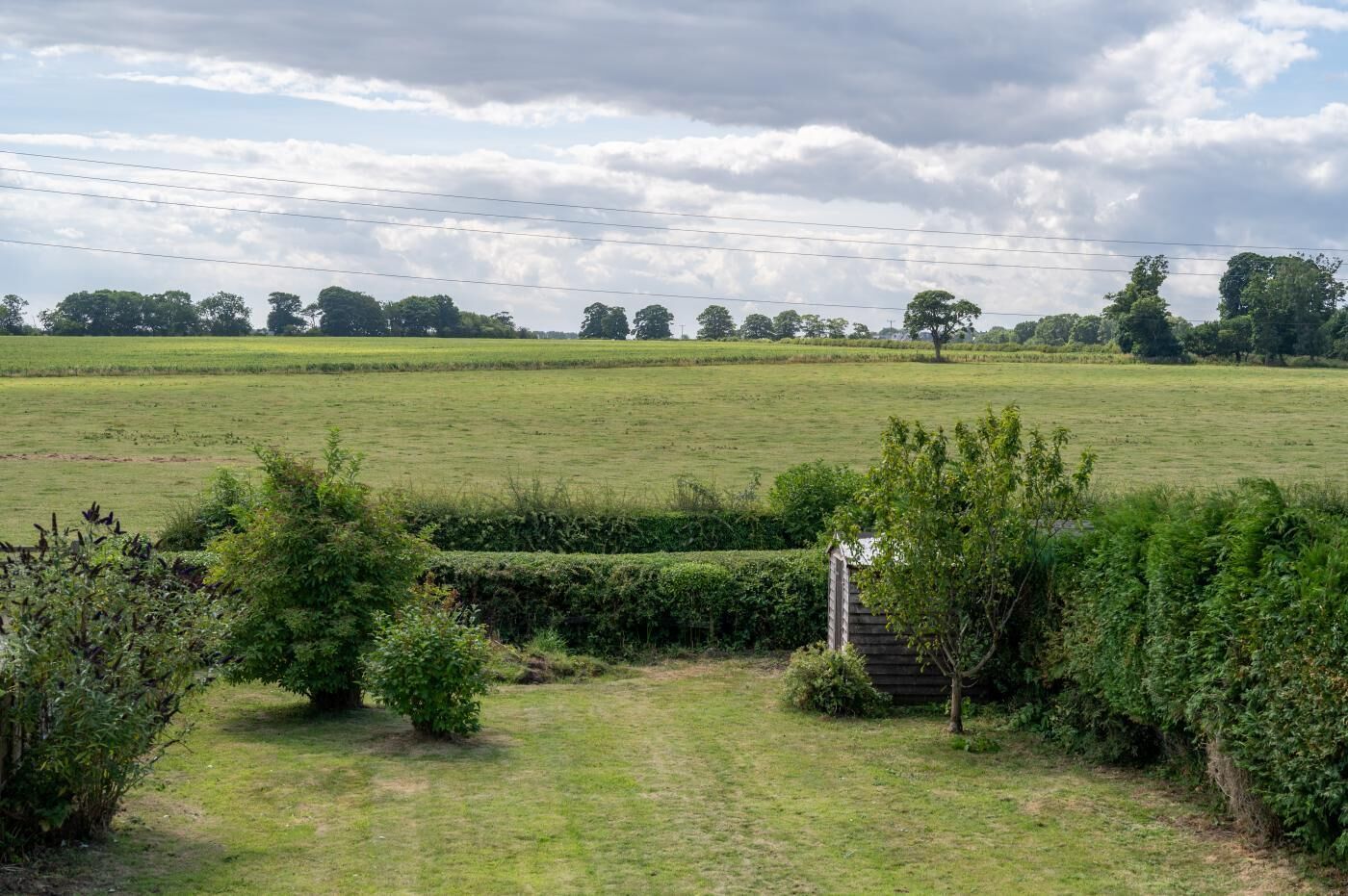 A rural landscape with a grassy field, a wooden gate, and a small structure in the foreground.