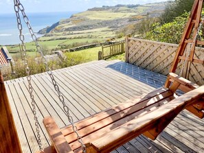 Una terraza de madera con un columpio y un banco, con vistas a un paisaje pintoresco.