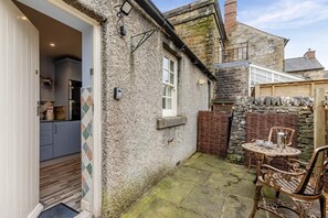 Un patio exterior acogedor con pared de piedra, una mesa de mimbre y una silla.