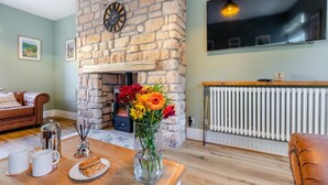 A cozy living room with a stone fireplace, a flat-screen TV mounted above it, and a dining area with a table set for two.