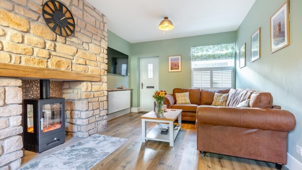 A cozy living room with a stone fireplace, a brown leather sofa, and a coffee table.