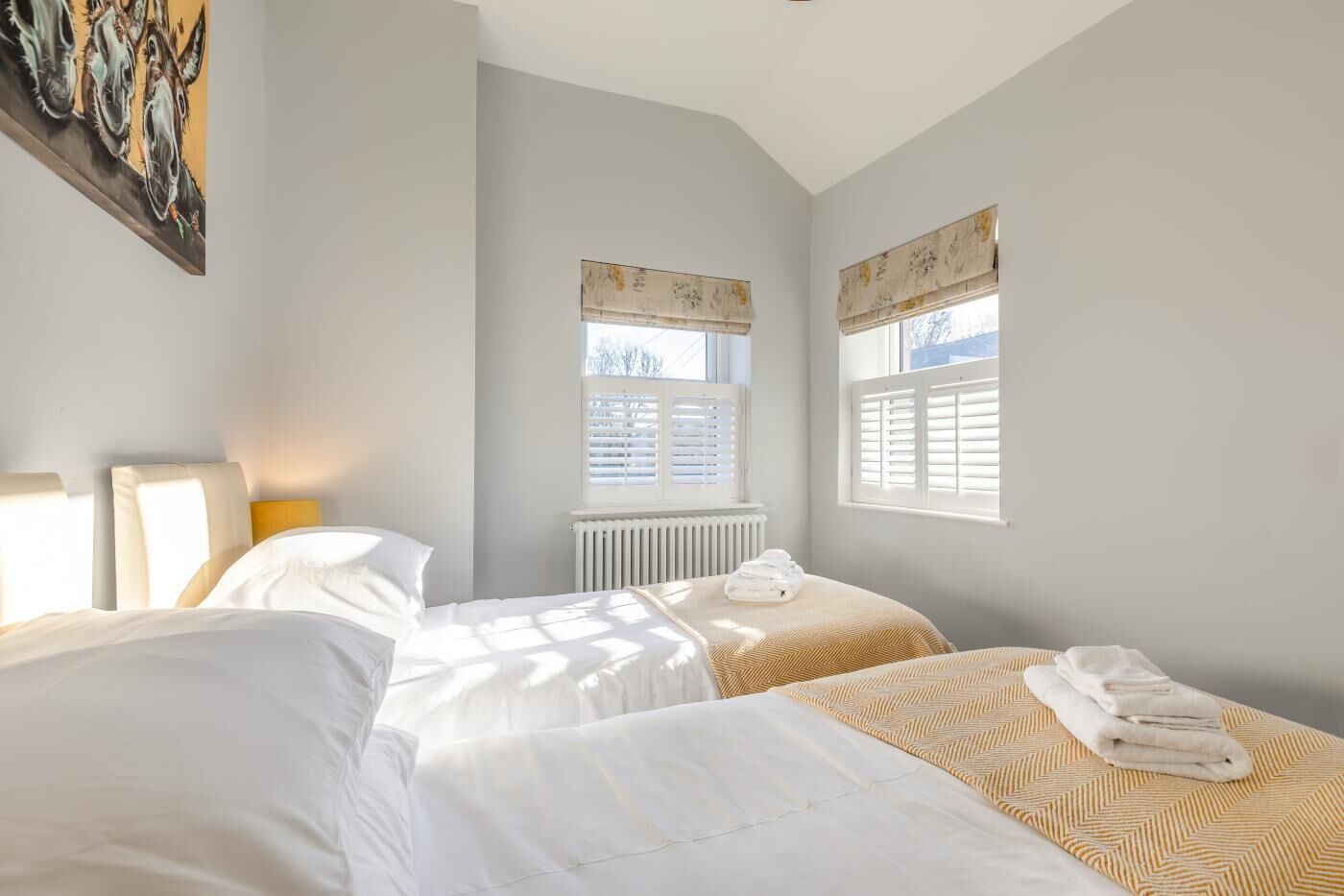 A hotel room with two beds, a radiator, and windows with shutters.
