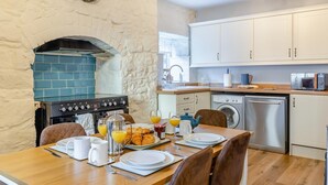 A kitchen with a stone wall, a stove, a washing machine, and a dining area with breakfast set.