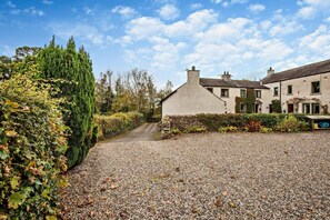 A gravel driveway leading to a house with a stone wall and a hedge on the left, and a row of houses on the right. - 2 Bed in Bassenthwaite (oc-ld171) (Bassenthwaite)