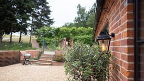 A brick building with a gravel patio, a barbecue grill, steps leading to a gate, and a potted plant. - 3 Bed in Ringsfield (oc-m33329) (Ringsfield)