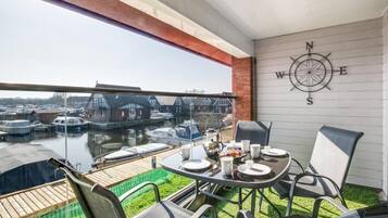 Un balcon avec une table dressée pour deux personnes, donnant sur une marina où l’on peut admirer des bateaux et des maisons.