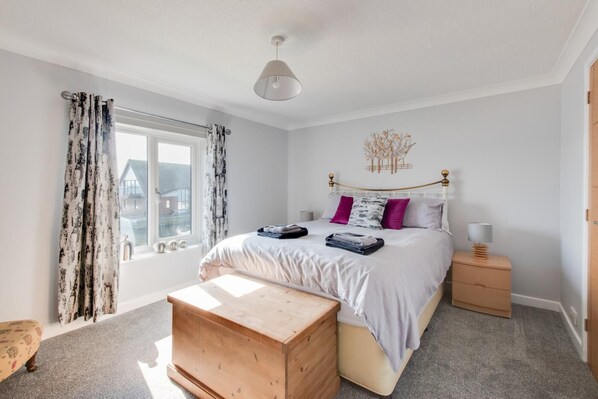 A bedroom with a bed, bedside tables, a wooden bench, and a window with curtains. - 2 Bed in Horning (oc-1860) (Horning)