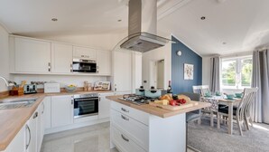 A modern kitchen with white cabinets, a central island with a gas stove, and a dining area with a table and chairs. - 2 Bed in Burnham Market (oc-2335) (Burnham Market)