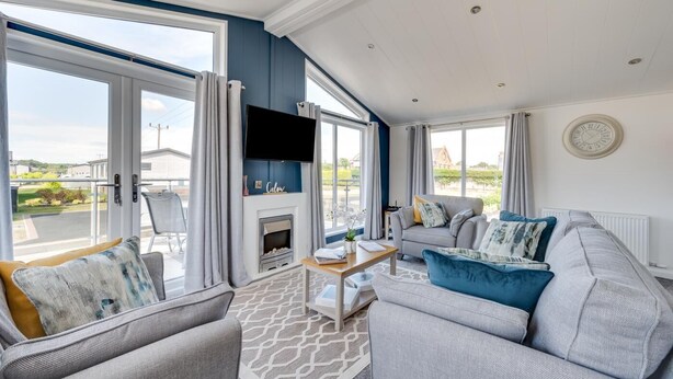 A spacious living room with a fireplace, comfortable seating, and large windows offering a view of the surrounding area. - 2 Bed in Burnham Market (oc-2335) (Burnham Market)