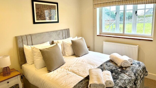 A neatly made bed with white and grey linens, a framed picture above it, and a window with curtains. - 4 Bed in Holkham (oc-h34081) (Holkham)