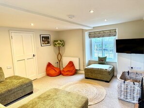Ein gemütliches Wohnzimmer mit einer Couch, einem Hocker und einem an der Wand befestigten Fernseher.