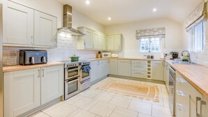 A modern kitchen with white cabinets, stainless steel appliances, and a large window. - 4 Bed in Holkham (oc-h34081) (Holkham)