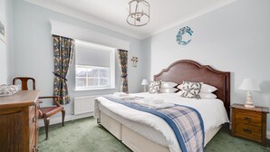 A bedroom with a bed, a wooden dresser, a chair, a nightstand, a lamp, a window with curtains, and a wall decoration. - 3 Bed in Holt (oc-2280) (Holt)