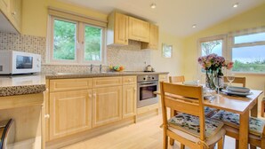 A kitchen with wooden cabinets, a microwave, an oven, and a dining area with a table and chairs. - 2 Bed in St. Merryn (oc-p00673) (Saint Merryn)