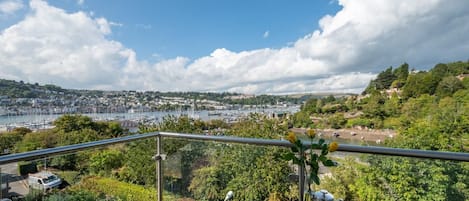 A balcony with a view of a marina, greenery, and a distant town.