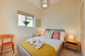 A neatly arranged bedroom with a bed, a chair, a bedside table, a lamp, a window with a view, and a radiator. - 2 Bed in Kingswear (oc-sdems) (Dartmouth)