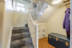Eine Treppe mit weißen Balustraden, ein dunkelbrauner Koffer mit Messingbeschlägen und ein Fenster mit weißem Rahmen.