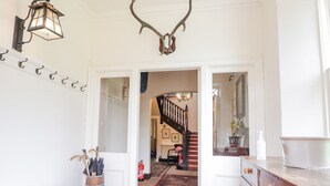 Een gang met een houten kast, een kapstok en een decoratie van een hertengewei.