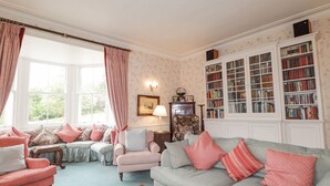 Een knusse woonkamer met een bank, fauteuils, een salontafel en een boekenplank vol boeken.
