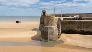 Ein Küstenstrand mit einem steinernen Leuchtturm und einem Boot im Sand.