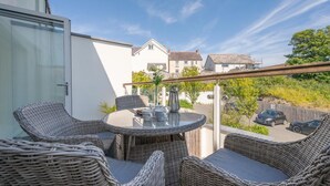 Ein Balkon mit Korbmöbeln, einem Glastisch und Blick auf eine Wohngegend.