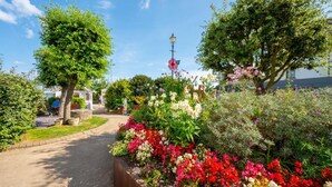 Ein Gartenpfad mit bunten Blumen, Bäumen und einer Lampe.