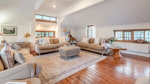 A spacious living room with a large sectional sofa, a coffee table, and a wooden floor. There are large windows providing natural light and a view of the outdoors. - 6 Bed in Englefield Green (oc-e34166) (Englefield Green)