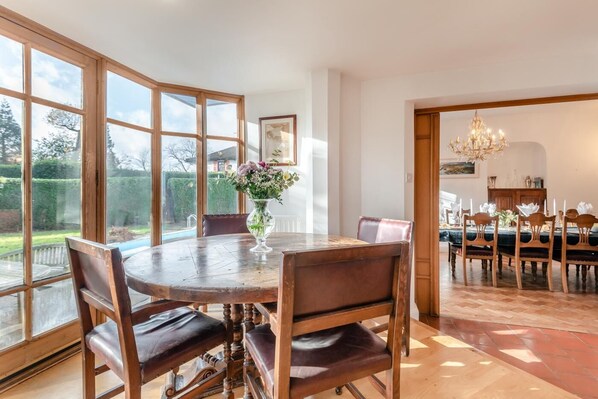 A dining area with a round table, wooden chairs, and a vase of flowers.