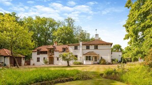 A two-story house with a garden in front, a small pond, and a clear sky. - 6 Bed in Englefield Green (oc-e34166) (Englefield Green)