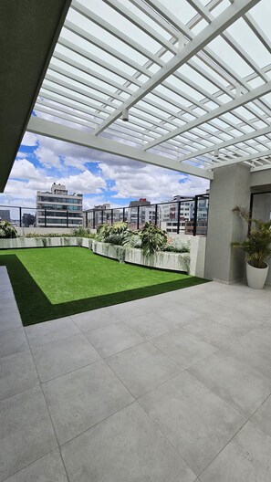 Terraza en la azotea con césped artificial, plantas en macetas y vista panorámica de la ciudad.