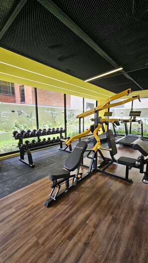 Un gimnasio con equipo de levantamiento de pesas, mancuernas, cintas de correr y suelo de madera.