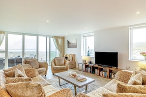 A spacious living room with wicker furniture, a flat-screen TV, and a bookshelf. - 3 Bed in Perranporth (oc-p00692) (Perranporth)