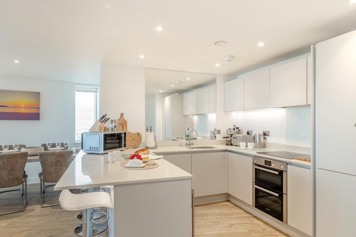 A modern kitchen with white cabinetry, a central island, and a dining area with chairs.