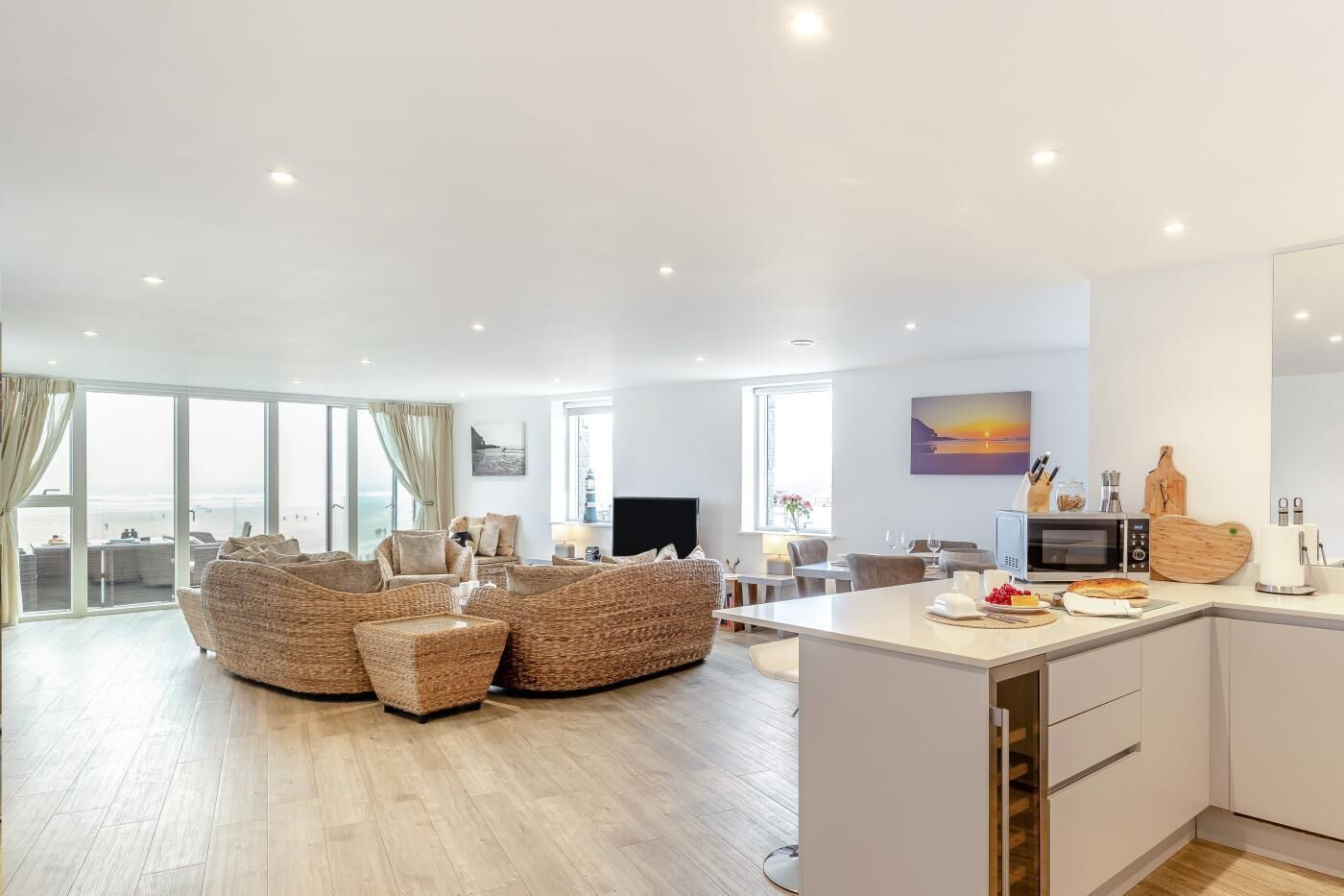 A modern living room with wicker furniture, a dining area, and a kitchen with a microwave and toaster.