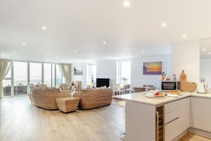 A modern living room with wicker furniture, a dining area, and a kitchen with a microwave and toaster. - 3 Bed in Perranporth (oc-p00692) (Perranporth)