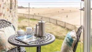 Un balcon avec une table préparée pour le thé, une vue sur la plage et un mur en briques.