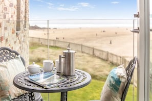A balcony with a table set for tea, a view of the beach, and a brick wall. - 3 Bed in Perranporth (oc-p00692) (Perranporth)