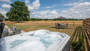 A hot tub in a backyard with a wooden fence, a table with chairs, and a large tree.
