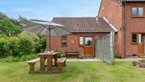 Une maison en briques avec un toit en tuiles, une table en bois avec des bancs, et un grand parasol.
